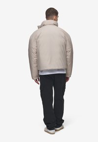Jachetă puffer bej cu guler înalt, croială supradimensionată și textură netedă. Asortată cu pantaloni cargo negri și adidași albi.