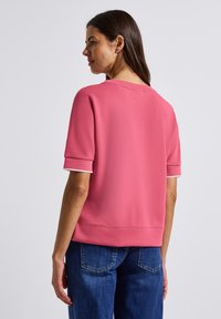 Sweatshirt rose à manches courtes avec un col rond, doté de bordures blanches sur les manches et d'une coupe décontractée. Texture lisse avec une couleur unie.