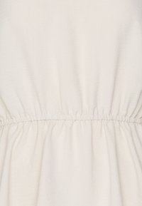 Light beige fabric with a textured surface, featuring gathering at the waist and soft, flowing drape. Smooth finish with minimal seams.