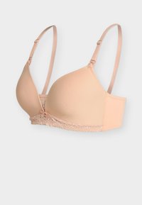 Beige vadderad behå med justerbara band och spetskant längs nederkanten, visad mot en ljus bakgrund.