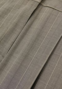 Lätt, texturerad tyg i en dämpad taupe-färg med vertikala randmönster och veck för en skräddarsydd look.