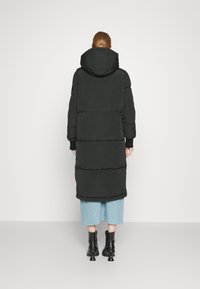 Svart vadderat täckjacka med huva, med en lång, rak design, räfflade manschetter och en slät textur, bärs över en jeanskjol och stövlar.