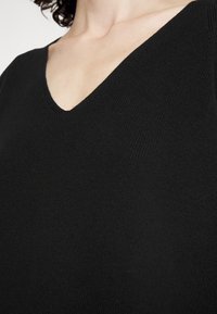 Zwarte v-hals top gemaakt van textuurgevoerde gebreide stof, met een diepe halslijn en een zachte uitstraling. De hoek richt zich op de halslijn en het borstgebied.