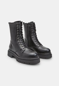 Stivali in pelle nera con lacci, dotati di un alto stivale, zip laterale, suole in gomma spessa e occhielli in metallo, caratterizzati da una superficie liscia e un design resistente.