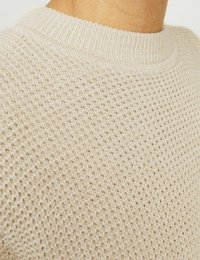 Maglione lavorato a maglia di un beige chiaro con un motivo testurizzato e un colletto a costine. La vista ravvicinata mette in evidenza i dettagli del tessuto e le cuciture.