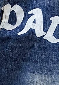 Denim fabric featuring bold white lettering. The design has a frayed texture with a gradient from dark to light blue. No other notable details.