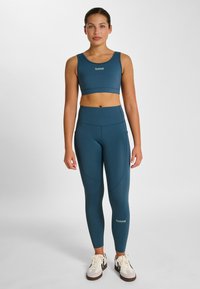 Sport-bh i blågrön färg och högmidjade leggings i slät, stretchig tygkvalitet, med sömdetaljer och en liten logga på midjebandet.