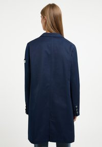 Navyblauwe jas met een klassiek ontwerp, voorzien van een enkele split, lange mouwen en knoopaccenten op de manchetten. Soepele stofstructuur.