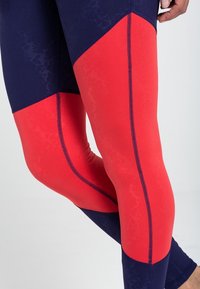 Högpresterande leggings med en kombination av marinblå och lysande röda paneler, slät yta och kontrasterande sömnadsdetaljer.