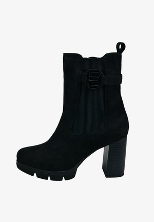 Bottine en daim noir avec un talon bloc, panneau latéral élastique ribbé et un accent logo noir circulaire. Semelle en caoutchouc texturé.