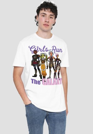 Man wearing white T-shirt with four animated female characters and text "Girls Run The Galaxy" in purple and pink letters.