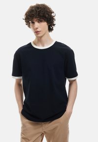 Granatowa koszulka z krótkim rękawem z kontrastującą kremową, prążkowaną kołnierzykiem i brzegami rękawów. Miękka tkanina, luźny krój, minimalistyczny design.