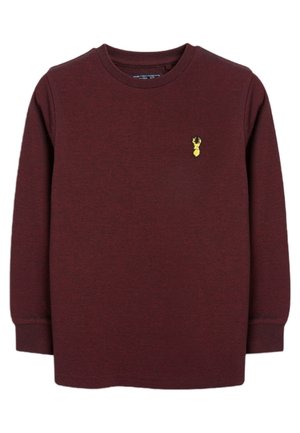 Langärmeliges bordeauxrotes Rundhalsshirt mit gerippten Bündchen und einem kleinen gelben Hirschkopf-Emblem auf der linken Brust.