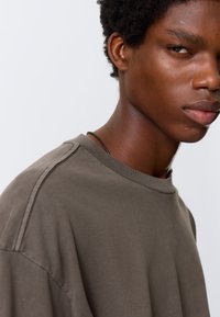 Groenbruin oversized katoenen T-shirt met een ribbelboord en gestikte schouderdetails. Glad materiaal met een relaxte pasvorm.