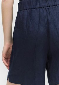 Linanin tummansinisiä shortseja, joissa on joustava vyötärö, sileä, hieman tekstuuri kangas ja sivuaukot helmassa.