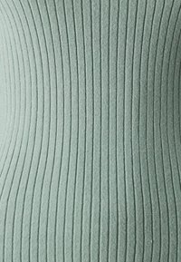 Prążkowany materiał dzianinowy w stonowanym zielonym kolorze, z pionowymi liniami i gładką fakturą, tworzący optycznie smukłą sylwetkę.