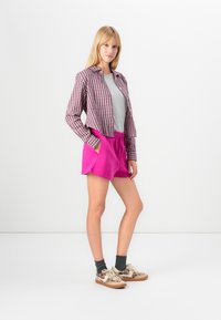 Avslappnad outfit med en croppad, rutig jacka i röd och vit, grå t-shirt och rosa shorts med resårmidja. Bärs med mönstrade sneakers.