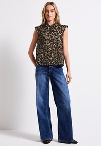 Khaki leopardí potisk bez rukávů s ohnutými rukávy, doplněný o široké modré džíny. Hladká textura, volný střih a jemný detail výstřihu.