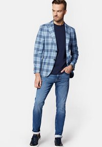 Jasnoniebieska marynarka w kratę z granatowymi akcentami, noszona na granatowej koszulce, zestawiona z niebieskimi dżinsami i czarnymi trampkami. Gładka tekstura, dopasowany krój.