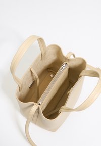 Beige leather tote bag with a smooth finish, featuring a spacious interior, a zippered pocket, and two short handles.