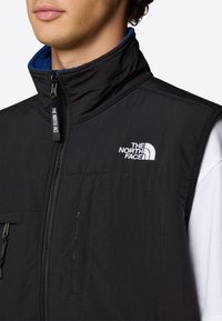 Czarna ocieplana kamizelka z wysokim kołnierzem, zamek błyskawiczny oraz dwiema przednimi kieszeniami. Logo "The North Face" jest haftowane na klatce piersiowej.