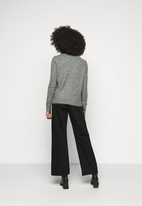 Szary sweter dzianinowy z okrągłym dekoltem, długimi rękawami, w połączeniu z czarnymi spodniami z wysokim stanem i szerokimi nogawkami oraz czarnymi botkami za kostkę.