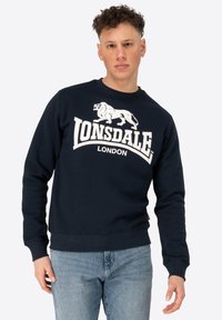 Navy blue sweatshirt with a crew neckline, featuring a large white lion logo and "LONSDALE LONDON" text. Made from a textured fabric.