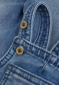 Close-up van blauwe denimstof met dubbele bruine knopen en gedetailleerde stiksels op een gevouwen kledinggedeelte.