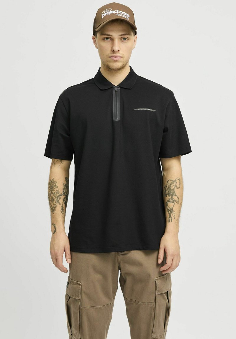 Zwarte polo met een ritskraag, korte mouwen en een subtiele logodetail op de borst. Gestyled met beige cargobroeken.