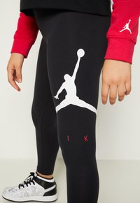 Czarne legginsy z białym logo Jumpman na udzie i czerwonymi akcentami. Noszone z czarno-białymi wzorzystymi sneakersami.