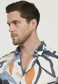 Chemise à manches courtes avec un motif abstrait multicolore en beige, marine, orange et bleu. Fabriquée en coton léger avec un col.