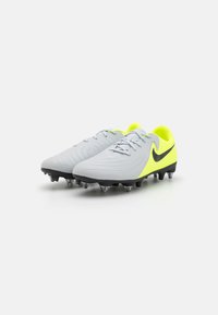 Grå fodboldstøvler med gule detaljer, struktureret overflade, sort Nike-logo og formede knopper til greb på kunstgræs. Snørebånd i lys grå.