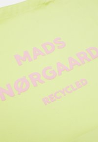 Tissu vert clair avec du texte rose en relief indiquant "MADS NØRGAARD RECYCLED" en diagonale sur la surface.