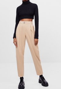 Svart strukturerad polo crop top kombinerad med beiga plisserade högmidjade byxor och kraftiga svarta plattformsskor.