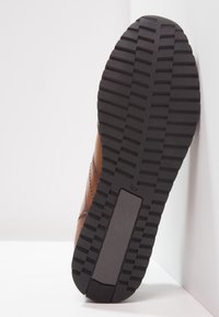 Braune Ledersneaker mit einer strukturierten schwarzen Gummisohle. Die Sohle hat tiefe Profilmuster für Traktion und einen verstärkten Fersenbereich.