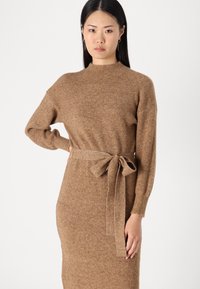 Abito lavorato a maglia marrone con maniche lunghe, scollo alto e cintura con fiocco in vita. Tessuto strutturato con un motivo a coste su tutta la superficie.