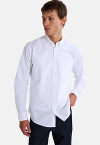 Chemise blanche à boutons avec col, manches longues et poche poitrine, fabriquée en tissu coton lisse, coupée dans un style décontracté.