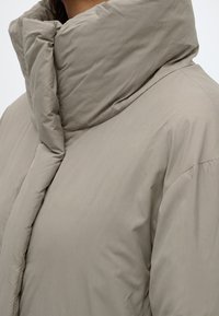 Gros plan d'une personne portant une doudoune beige clair avec un col rembourré haut qui couvre le cou.