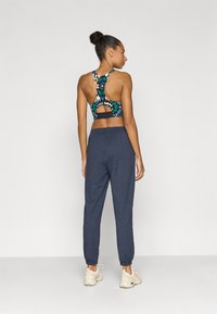 Αθλητικό σουτιέν με πολύχρωμο αφηρημένο σχέδιο, που διαθέτει κοψίματα στην πλάτη. Συνδυάζεται με γκρι στενά φαρδιά φόρμα και ανοιχτόχρωμα αθλητικά παπούτσια.