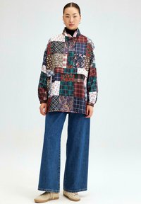 Patchwork jas met verschillende patronen in marineblauw, bordeaux en bloemmotieven, met een hoge kraag en een losse pasvorm, gecombineerd met wijde denim broek.