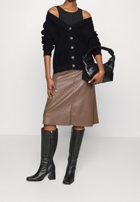 Czarny dzianinowy kardigan na guziki, brązowa skórzana spódnica midi oraz czarne skórzane kozaki do kolan na kwadratowym obcasie. Strukturalna czarna torebka.