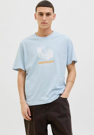 T-shirt en coton bleu clair à manches courtes, comportant un design graphique blanc et orange incluant des feuilles de palmier et le mot "ORIGINALS."