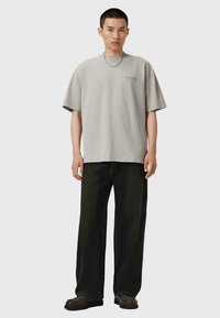 Lichtgrijs oversized T-shirt met korte mouwen, voorzien van een klein logo. Gecombineerd met donkere wijde jeans en zwarte schoenen.