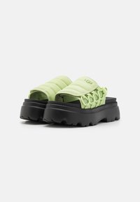 Chanclas acolchadas verdes con suela negra gruesa, que presentan un detalle de tiras trenzadas y un upper texturizado para un diseño contemporáneo.
