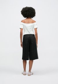 Ελαφρύ πράσινο τοπ με ανοιχτούς ώμους, σε συνδυασμό με μαύρες denim κουλότες, με ίσια γραμμή και μήκος μέχρι τον αστράγαλο, με πίσω τσέπες.