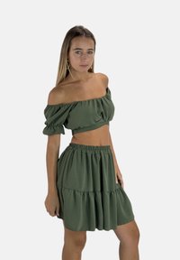 Top verde con hombros descubiertos y mangas abullonadas combinado con una falda verde de volantes; hecho de tela suave con un acabado texturizado.