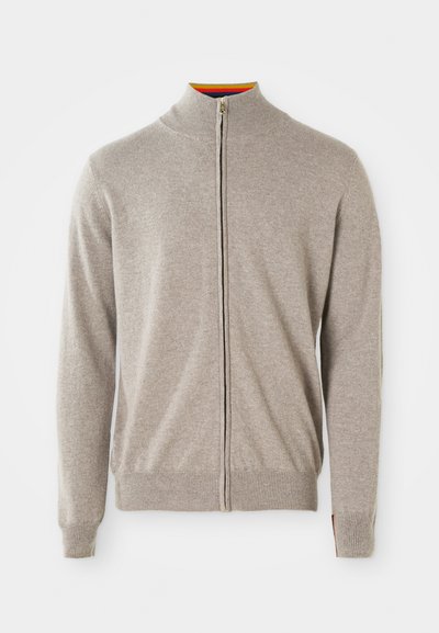 Stickad zip-sweater i ljusgrått. Har hög krage, ribbade ärmslut och fåll. Inuti kragen finns en färgglad accent. Mjuk textur.