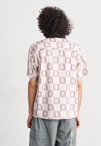 Short-sleeved shirt in light beige with a repeated purple square pattern. Made of lightweight fabric with a relaxed fit and a straight hem.