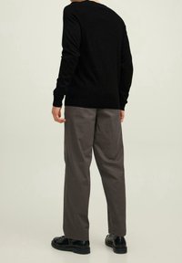 Pull noir à encolure ronde, accompagné d'un pantalon gris ample et de chaussures noires, présentant une texture lisse et un design simple.