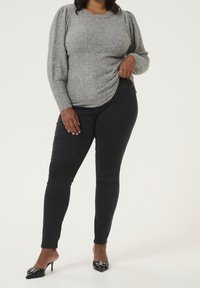 Grauer Pullover mit strukturiertem Stoff, Puffärmeln und abgerundetem Saum, kombiniert mit schwarzen Skinny-Jeans und schwarzen spitzen High Heels.